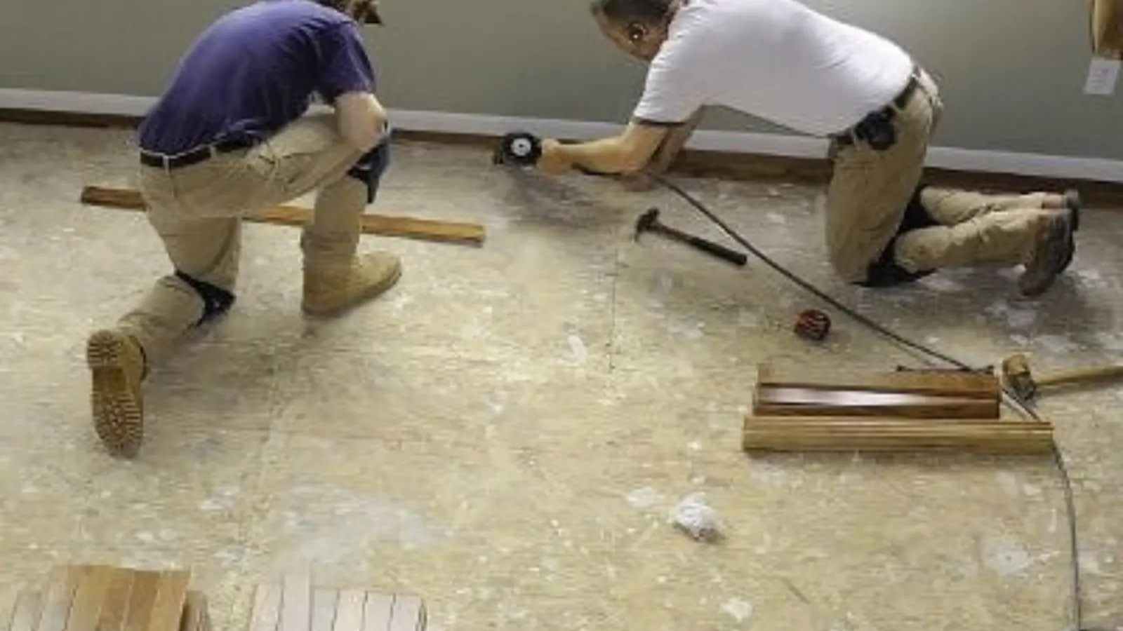 Two technicians kneeling on a wet floor and lifting damaged flooring boards