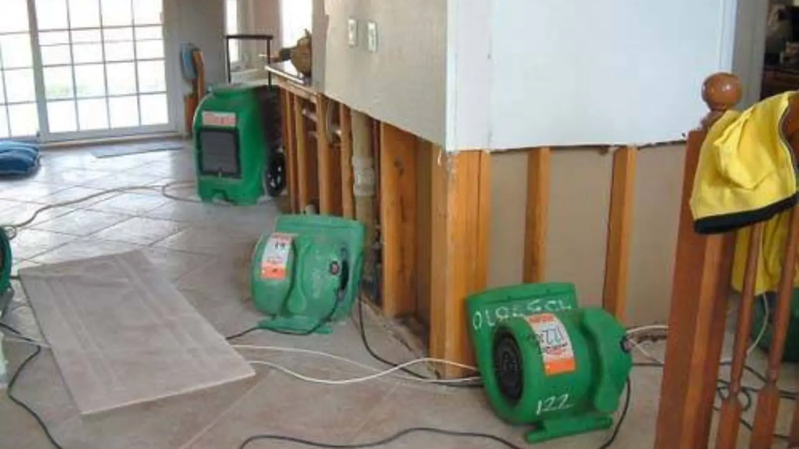 Green air movers drying a room with the lower wall sections cut away to show the framing