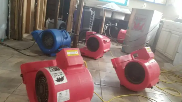 Red and blue air movers running on a wet tile floor to dry the room